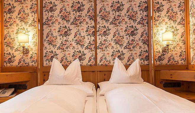 A cozy bedroom with two single beds and a floral wall pattern. The warm wooden details and soft light sources create an inviting atmosphere. - Art & Relax Hotel Bergwelt - Obergurgl 