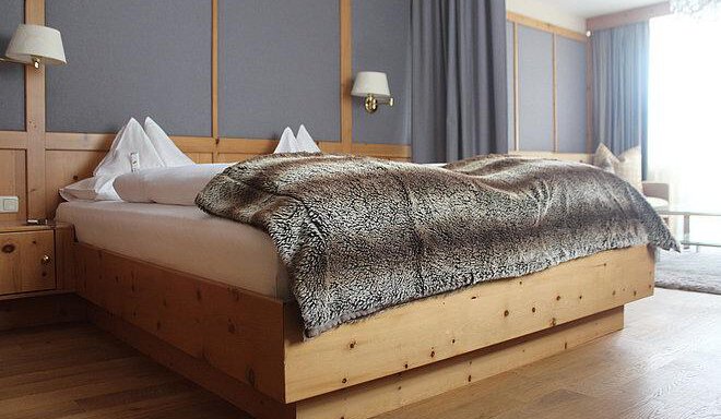 A cozy bedroom with a large bed and a soft throw. The walls are done in warm wood and gray tones. - Art & Relax Hotel Bergwelt - Obergurgl 