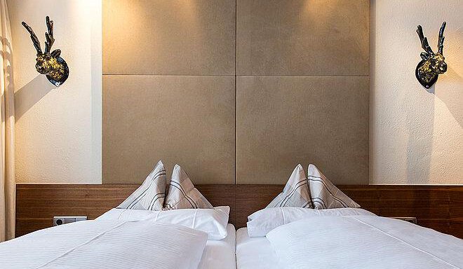 A modern bedroom with two single beds and elegant bedding. Decorative wall objects hang on the walls. - Art & Relax Hotel Bergwelt - Obergurgl 