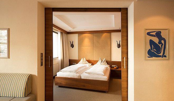 A modern bedroom with two beds and soft lighting. In the background, there is a couch and a piece of art on the wall. - Art & Relax Hotel Bergwelt - Obergurgl 