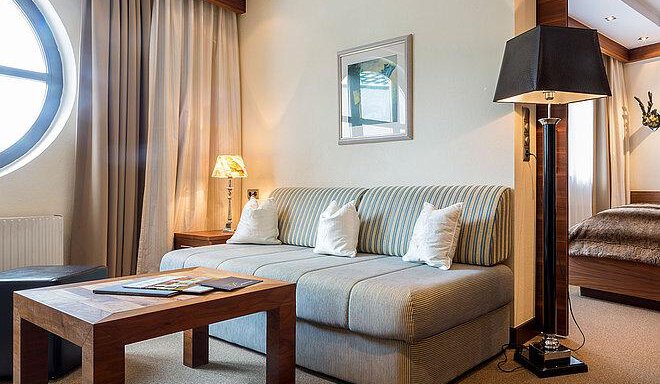 An elegant living room with a cozy sofa and a wooden coffee table. Large windows provide plenty of daylight and an inviting atmosphere. - Art & Relax Hotel Bergwelt - Obergurgl 