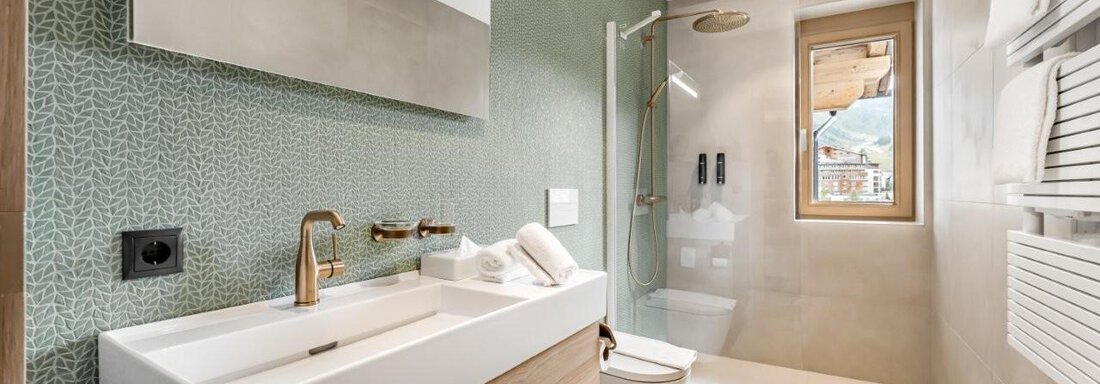 Ein modernes Badezimmer mit eleganten Armaturen und einer stilvollen Kombination aus grünen und neutralen Tönen. Es gibt eine große Dusche, ein Waschbecken und Handtuchhalter an der Wand. - Chalet Obergurgl luxury apartments - Obergurgl 