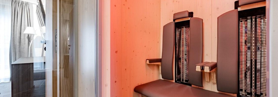 Eine moderne Infrarotkabine mit Holzverkleidung und zwei Sitzen. Im Hintergrund ist ein heller Raum mit Fenster und Möbeln zu sehen. - Chalet Obergurgl luxury apartments - Obergurgl 