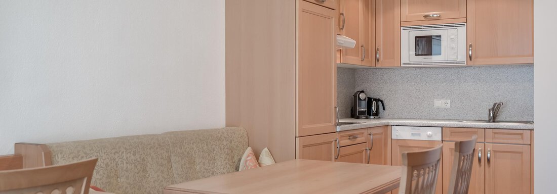 A bright kitchen with modern wooden furniture. There is a dining table and a cozy seating area. - Ferienwohnung de Luxe Alpenresidenz am Mühlbach - Obergurgl 