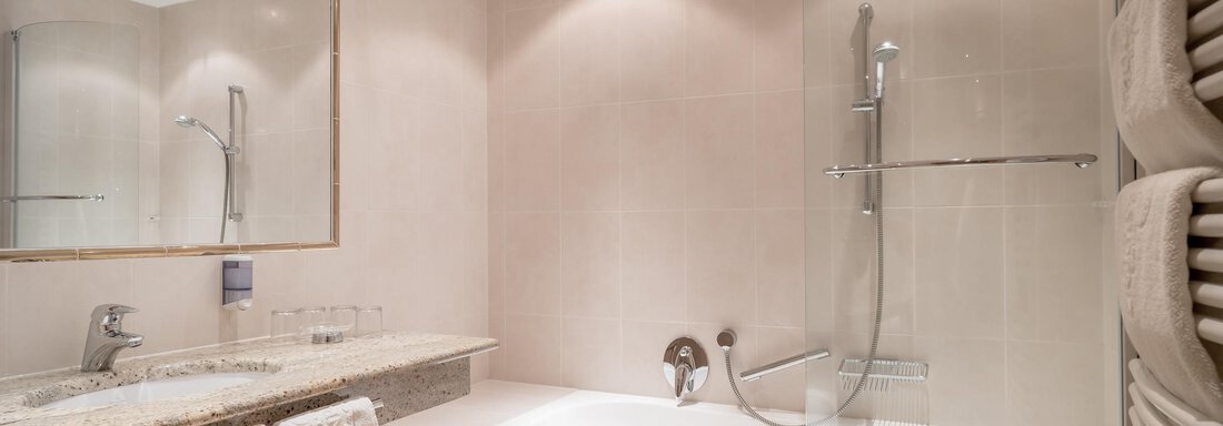 A modern bathroom with a bathtub and a shower. The walls are in neutral tones and there is a large mirror. - Ferienwohnung de Luxe Alpenresidenz am Mühlbach - Obergurgl 