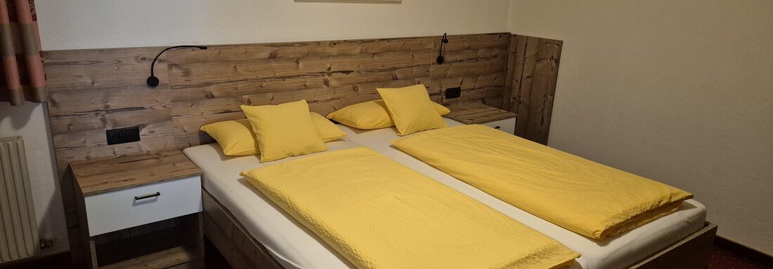 A cozy bedroom with a large bed and yellow blankets. The walls are made of wood and the decor is simple and modern. - Ferienwohnung Fabian - Obergurgl 