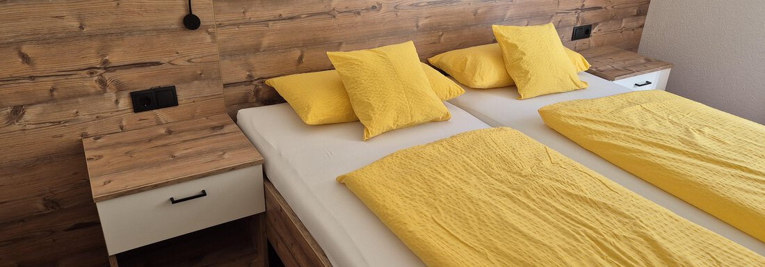 A cozy bedroom with two single beds and yellow bedding. The walls are made of wood and there is a nightstand next to one bed. - Ferienwohnung Fabian - Obergurgl 