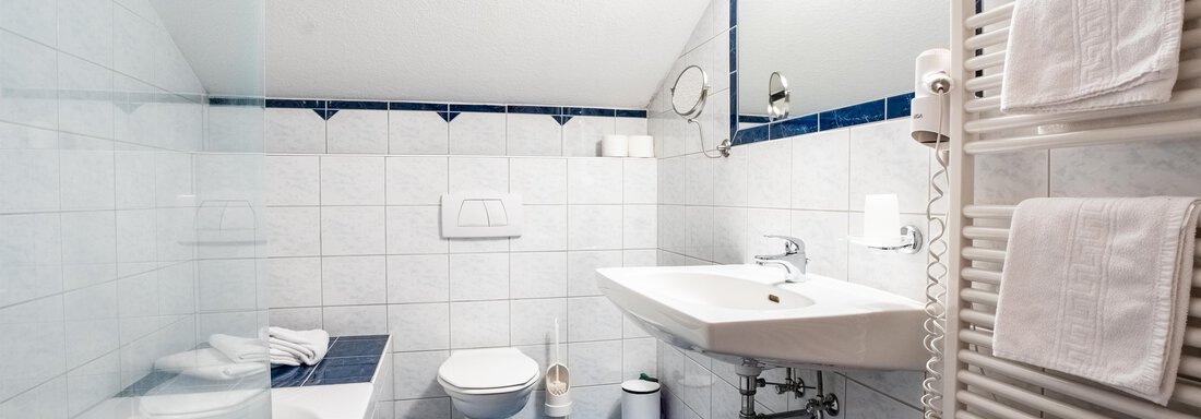 A modern bathroom with a bathtub and a sink. The walls are light tiled, and there are towels on the wall. - Ferienwohnung Romana - Obergurgl 