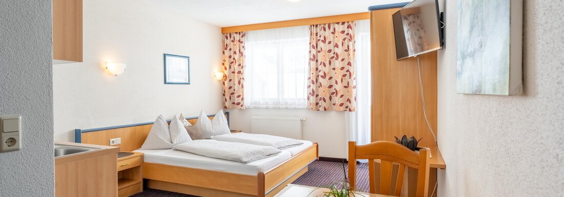 A bright room with two single beds and a small table. The windows are adorned with light curtains and there is a television on the wall. - Ferienwohnung Romana - Obergurgl 