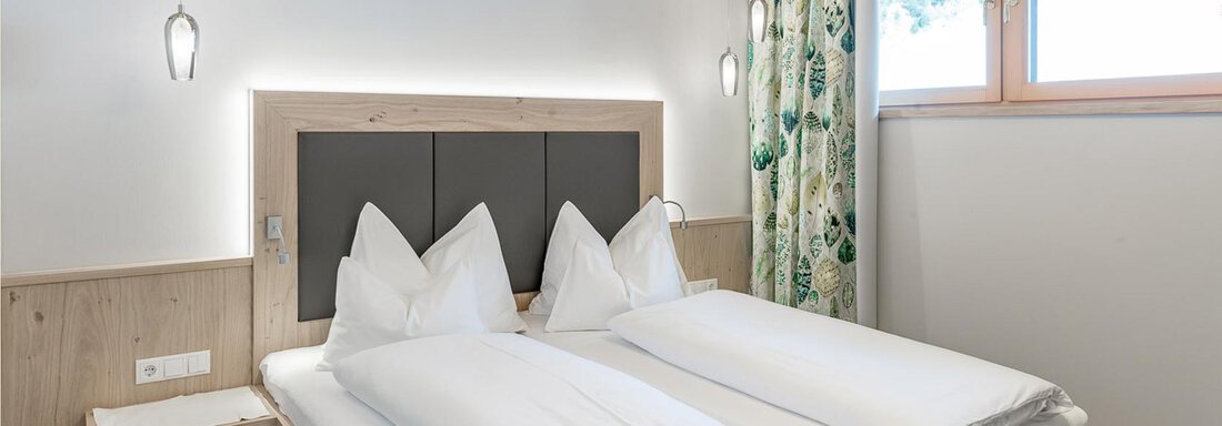 Ein gemütliches Zimmer mit zwei Einzelbetten und modernen Leuchten. Große Fenster mit Vorhängen sorgen für viel Tageslicht. - Skihotel Haus Gurgl - Obergurgl 