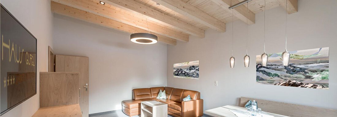 Ein modernes Wohnzimmer mit Holzdecke und gemütlicher Sitzecke. Der Raum ist hell und einladend mit einem Tisch und stilvollen Lampen. - Skihotel Haus Gurgl - Obergurgl 
