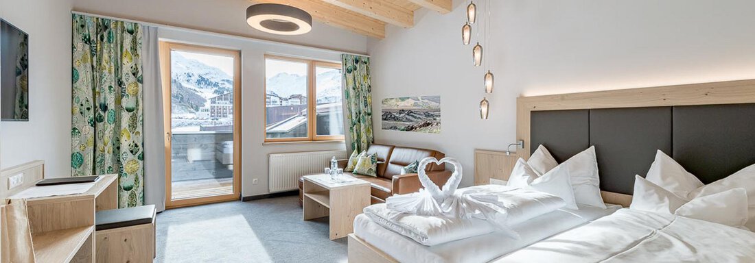 Ein modernes Hotelzimmer mit Holzdecken und einem großen Fenster. Es verfügt über ein Doppelbett, einen Sitzbereich und eine gemütliche Einrichtung. - Skihotel Haus Gurgl - Obergurgl 