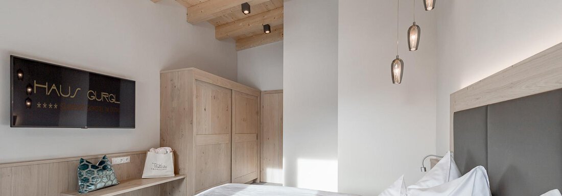 Ein modernes Schlafzimmer mit zwei Einzelbetten und Holzdekor. Die Wände sind hell gestrichen und die Beleuchtung sorgt für eine gemütliche Atmosphäre. - Skihotel Haus Gurgl - Obergurgl 