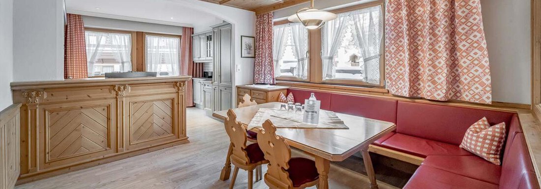 Ein gemütlicher Essbereich mit einem Holztisch und roten Sitzen. Die Fenster sind durch Vorhänge dekoriert und der Raum wirkt hell und einladend. - Skihotel Haus Gurgl - Obergurgl 