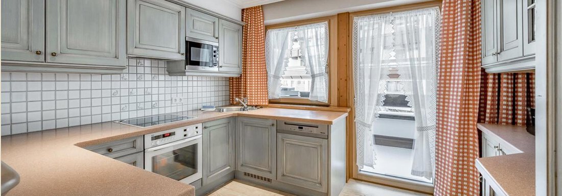 Eine moderne Küche mit grauen Schränken und Holzdetails. Große Fenster lassen viel Licht herein und schaffen eine einladende Atmosphäre. - Skihotel Haus Gurgl - Obergurgl 