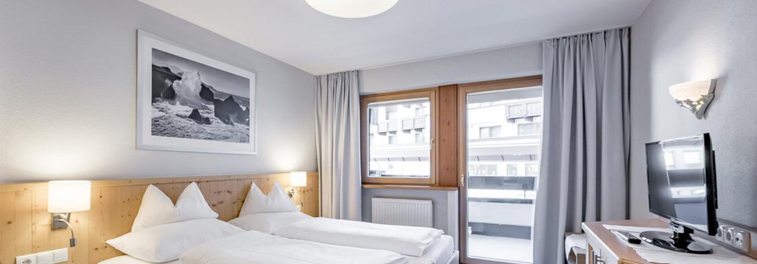 Ein modernes Hotelzimmer mit zwei Einzelbetten und Holzdetails. Der Raum hat große Fenster mit Blick auf einen Balkon und ist hell und freundlich gestaltet. - Skihotel Haus Gurgl - Obergurgl 