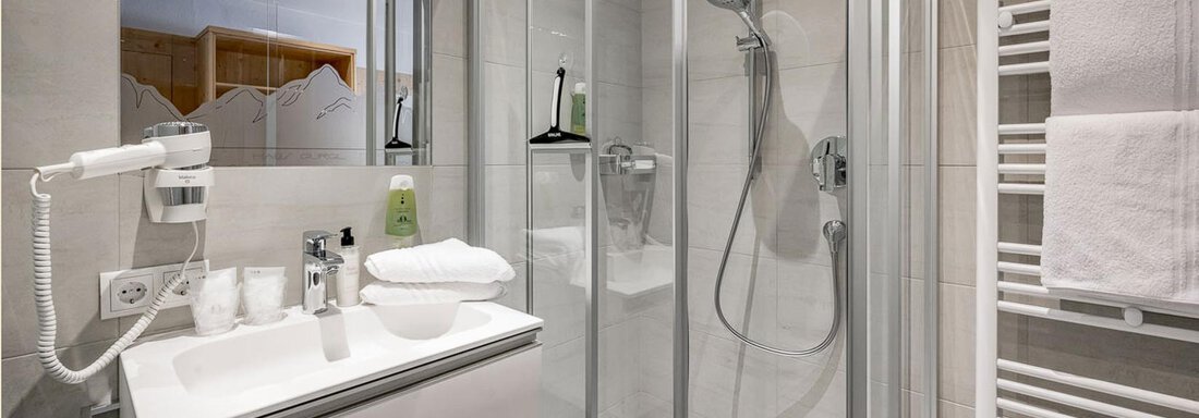 Ein modernes Badezimmer mit einer Dusche und einem Waschbecken. Weiße Handtücher und Pflegeprodukte sind auf der Ablage sichtbar. - Skihotel Haus Gurgl - Obergurgl 