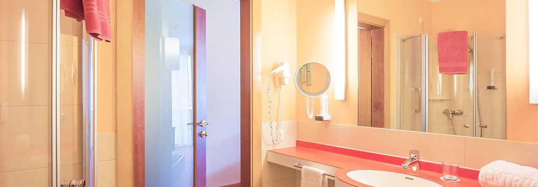 A modern bathroom with a bright color scheme. There is a shower, a mirror, and a sink with towels. - Vivea 4* Hotel Umhausen im Ötztal - Umhausen