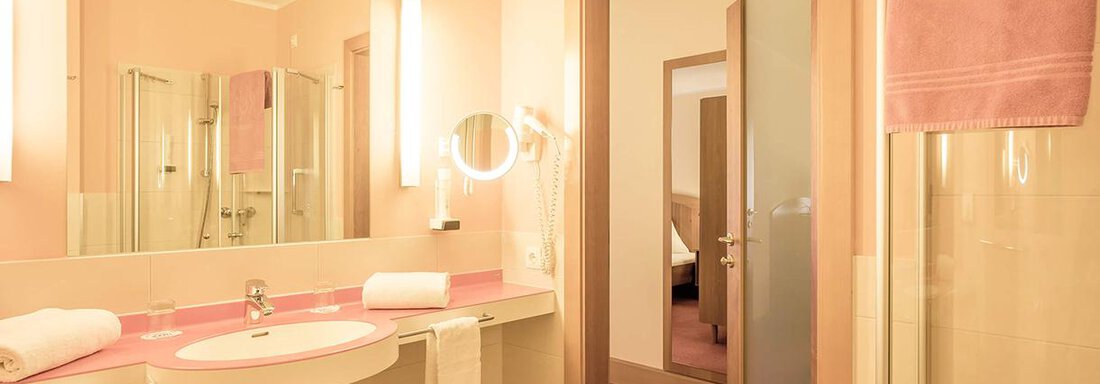 A modern bathroom with pink walls and a sink. In the background, a door to another room is visible. - Vivea 4* Hotel Umhausen im Ötztal - Umhausen