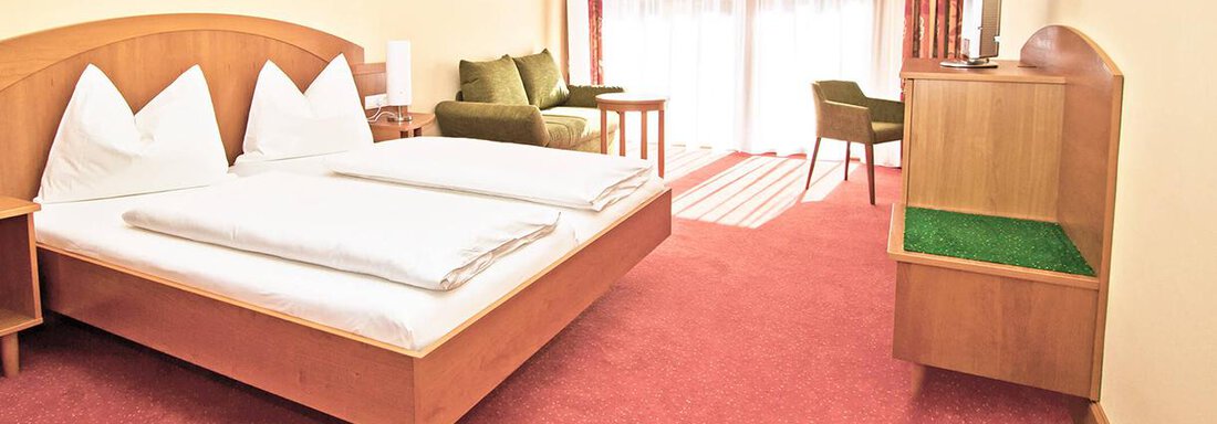 A cozy bedroom with a double bed and two comfortable armchairs. Large windows provide plenty of daylight and a view of the outdoors. - Vivea 4* Hotel Umhausen im Ötztal - Umhausen