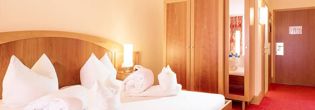 A cozy hotel room with a large bed and bright walls. The decor includes wooden cabinets and a warm, inviting atmosphere. - Vivea 4* Hotel Umhausen im Ötztal - Umhausen