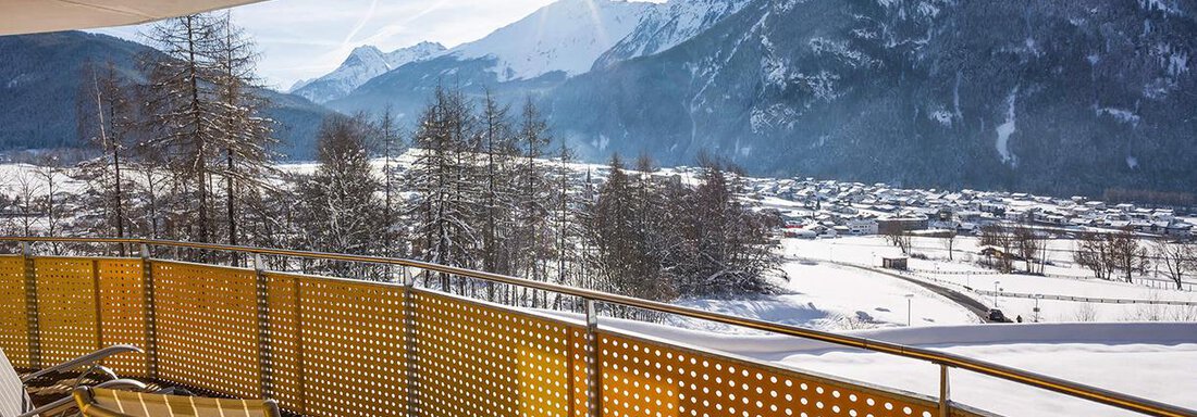 A balcony with two lounge chairs and a view of snow-covered mountains. The sun is shining over the picturesque Alpine landscape. - Vivea 4* Hotel Umhausen im Ötztal - Umhausen