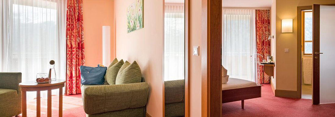 A cozy room with a green sofa and a small table. Large windows let in plenty of daylight and give the room a bright atmosphere. - Vivea 4* Hotel Umhausen im Ötztal - Umhausen