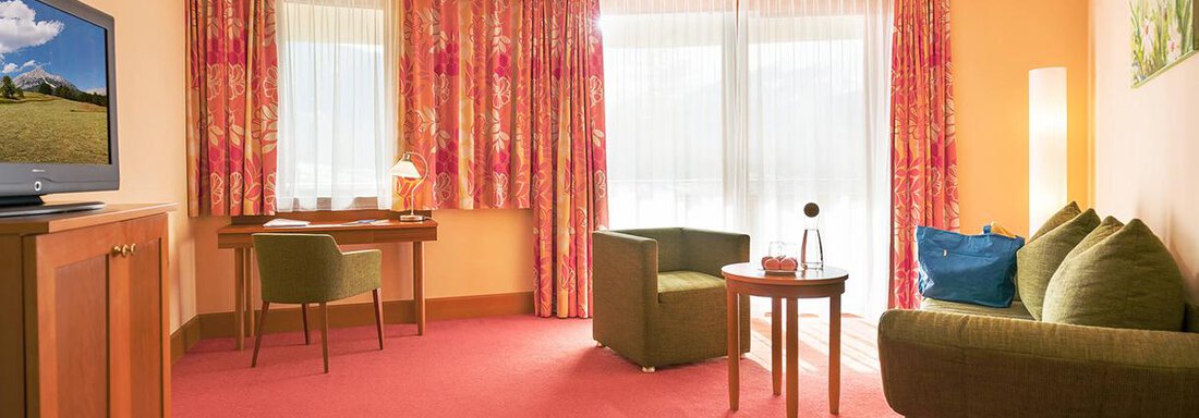 A cozy room with a green sofa and a small table. Bright curtains let in plenty of daylight. - Vivea 4* Hotel Umhausen im Ötztal - Umhausen