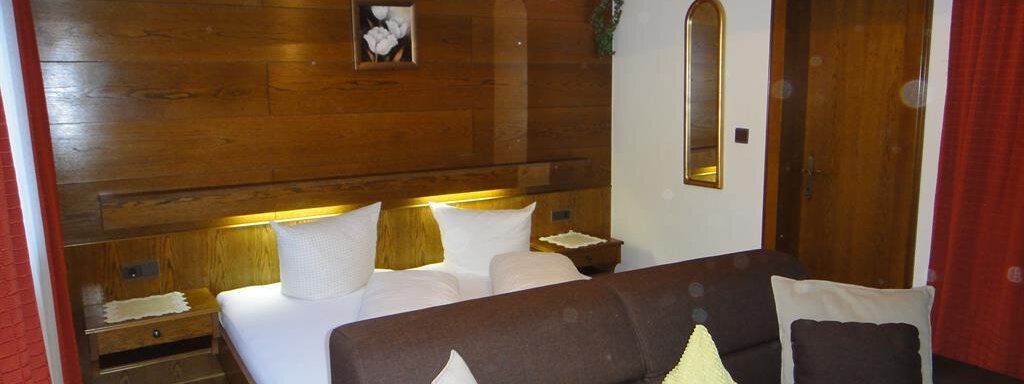 A cozy room with wooden paneling, a double bed, and a sofa. There are warm colors and soft light, creating an inviting atmosphere. - Haus Elisabeth - Vent