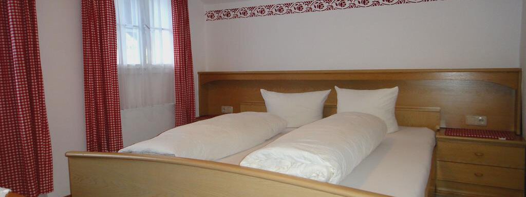 A cozy bedroom with two single beds and bright red curtains. The room features warm wooden decor and an inviting atmosphere. - Haus Elisabeth - Vent