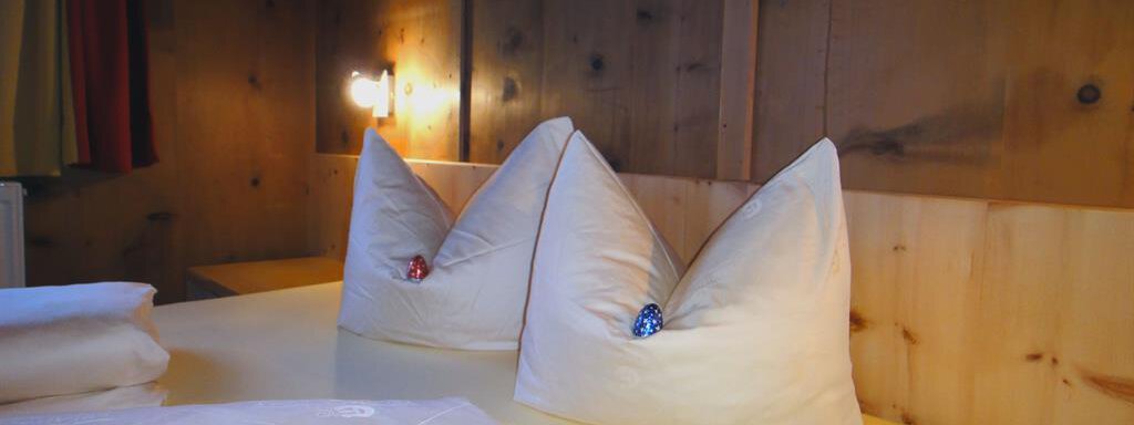 A cozy bedroom with wooden paneling. Two decorative pillows in the shape of hats on the bed. - Haus Elisabeth - Vent