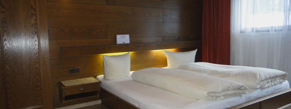 A modern bedroom with a wood design. The room is bright and cozy, with a large bed and a window that lets in daylight. - Haus Elisabeth - Vent