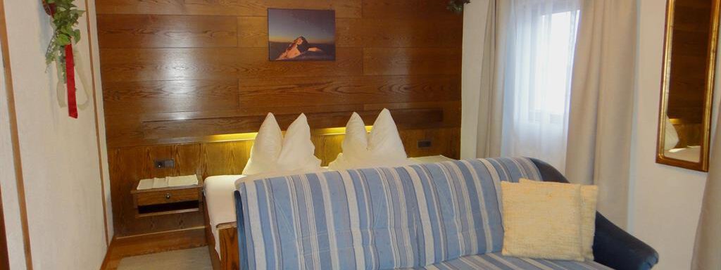A cozy hotel room with a double bed and a blue couch. The wooden paneling and soft lighting create an inviting atmosphere. - Haus Elisabeth - Vent