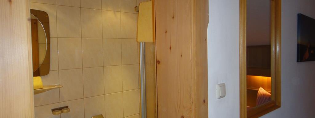 A small bathroom with a shower, a sink, and a toilet. The walls are tiled in light colors and there is a mirror. - Haus Elisabeth - Vent