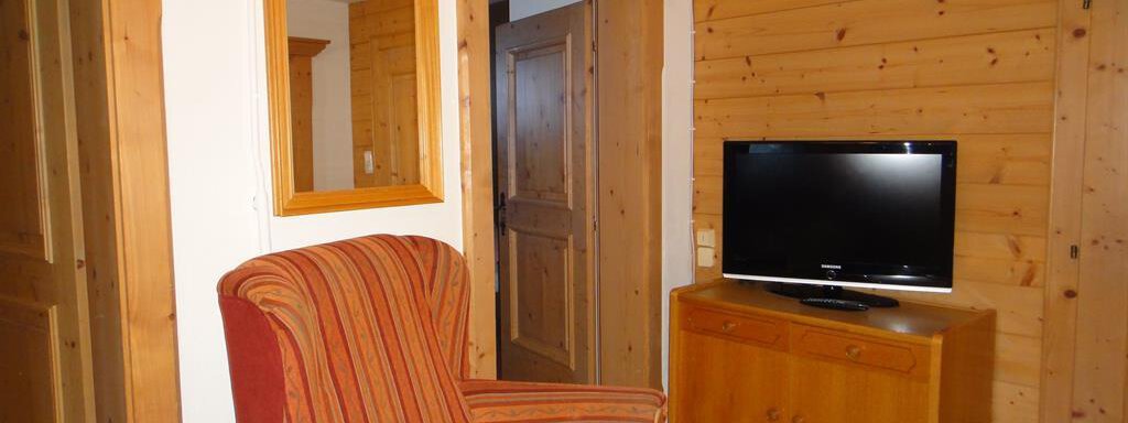 A cozy living space with a red armchair, a television, and wood-paneled walls. The room feels warm and inviting. - Haus Elisabeth - Vent