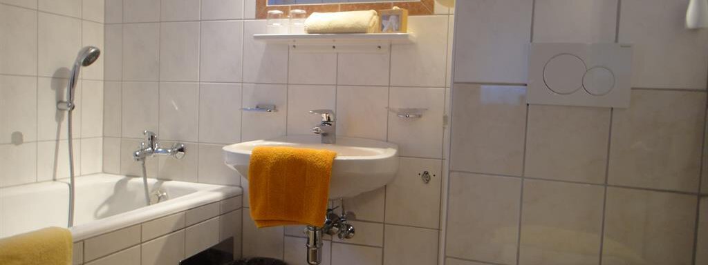 A modern bathroom with white tiles and a bathtub. Yellow towels are placed on the sink and the toilet. - Haus Elisabeth - Vent
