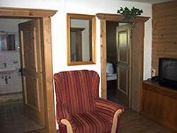 A cozy living space with a striped armchair and wooden doors. In the background, a television and other rooms are visible. - Haus Elisabeth - Vent