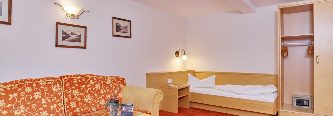 A cozy hotel room with a sofa and a table. In the background, a wardrobe and a single bed can be seen. - Hotel Vent - Vent